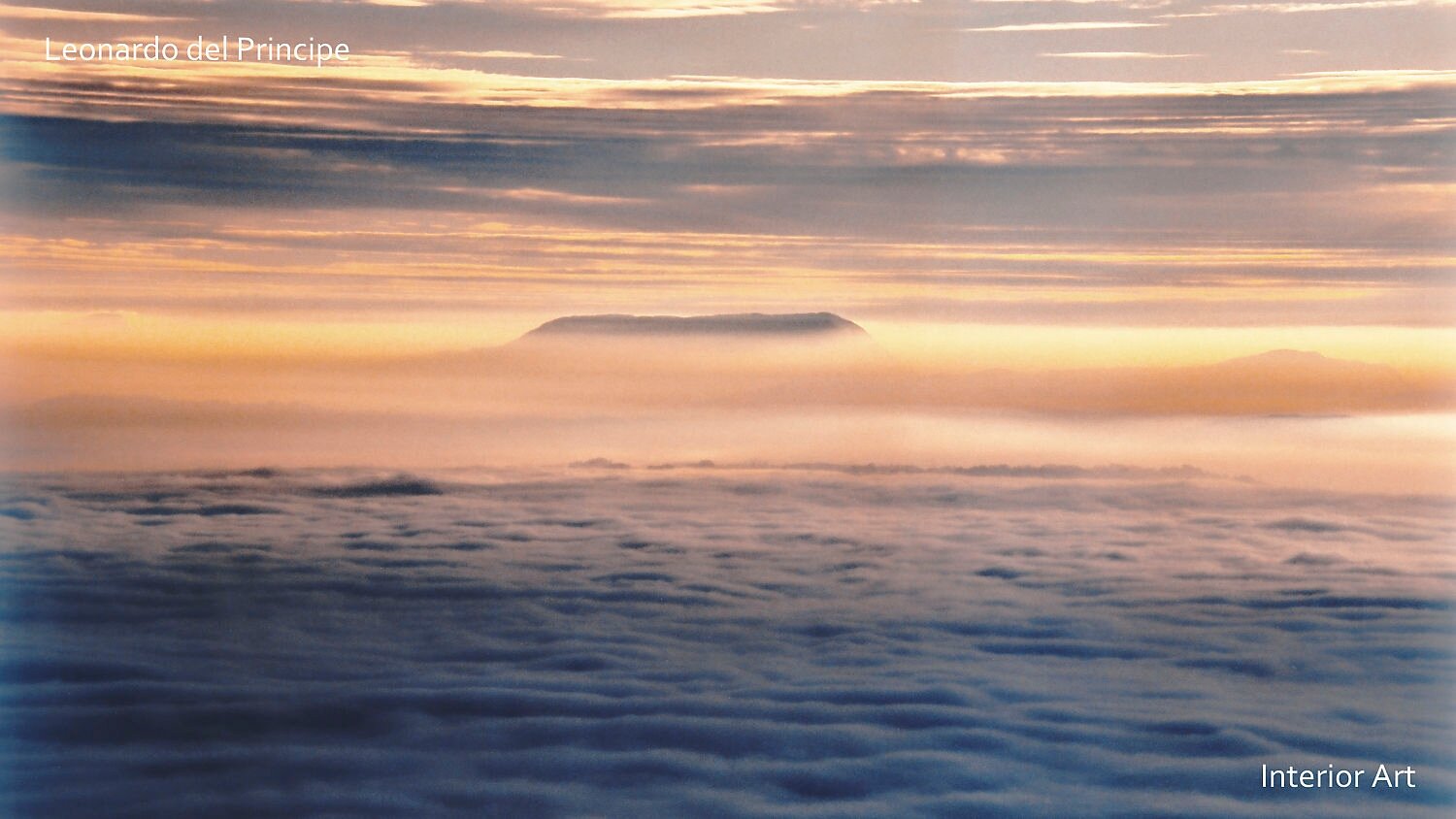 PUMO02 A vast sea of soft clouds glows under a golden sunrise, with a distant mountain peak visible on the horizon. The scene conveys tranquility and majesty.