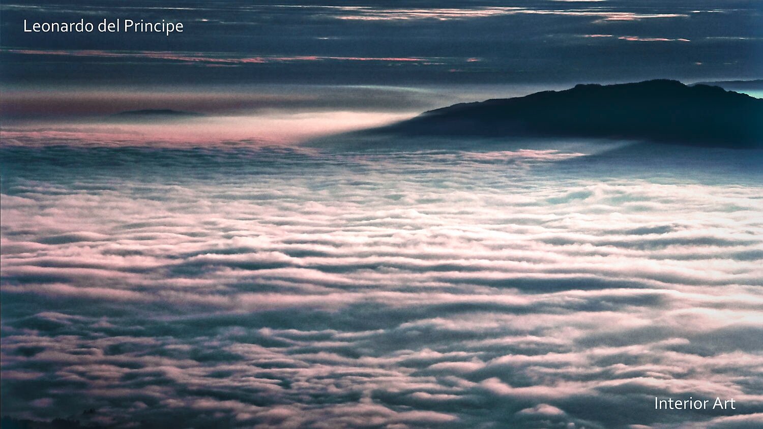 PUMO04 A serene landscape shows a sea of clouds bathed in soft pink and blue hues, with a dark mountain silhouette in the background under a colorful sky.